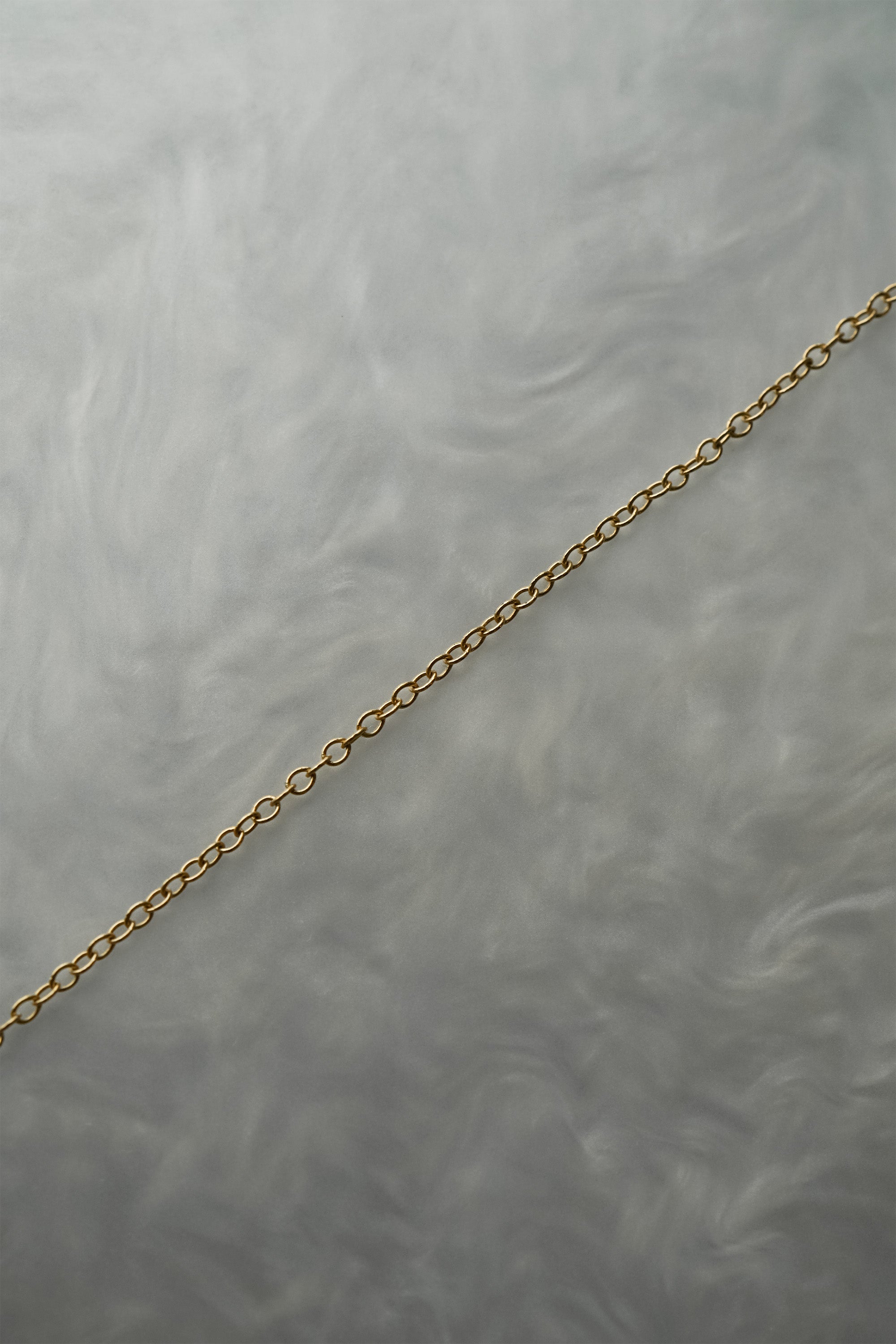 1.4mm cable chain with smooth oval links in solid 14k gold, perfect for wearing on its own or with charms or pendants. The chain is against a grey background with swirling patterns.