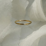 A stock photo of Laurie Fleming Jewellery's plain solid gold "Myrtle" band, a 1.4mm wide stacking ring/wedding band, handmade in Toronto. The ring is standing on its own surrounded by pieces of raw white silk.