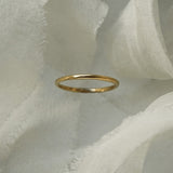 A stock photo of Laurie Fleming Jewellery's plain solid gold "Myrtle" band, a 1.4mm wide stacking ring/wedding band, handmade in Toronto. The ring is standing on its own surrounded by pieces of raw white silk.