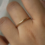 A stock photo of Laurie Fleming Jewellery's plain solid gold "Myrtle" band, a 1.4mm wide stacking ring/wedding band, handmade in Toronto. The ring is worn on a hand with a light grey background.