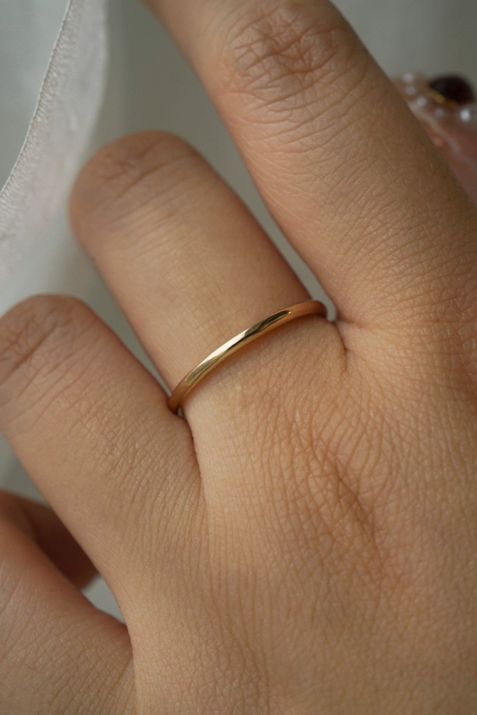 A stock photo of Laurie Fleming Jewellery's plain solid gold "Myrtle" band, a 1.4mm wide stacking ring/wedding band, handmade in Toronto. The ring is worn on a hand with a light grey background.