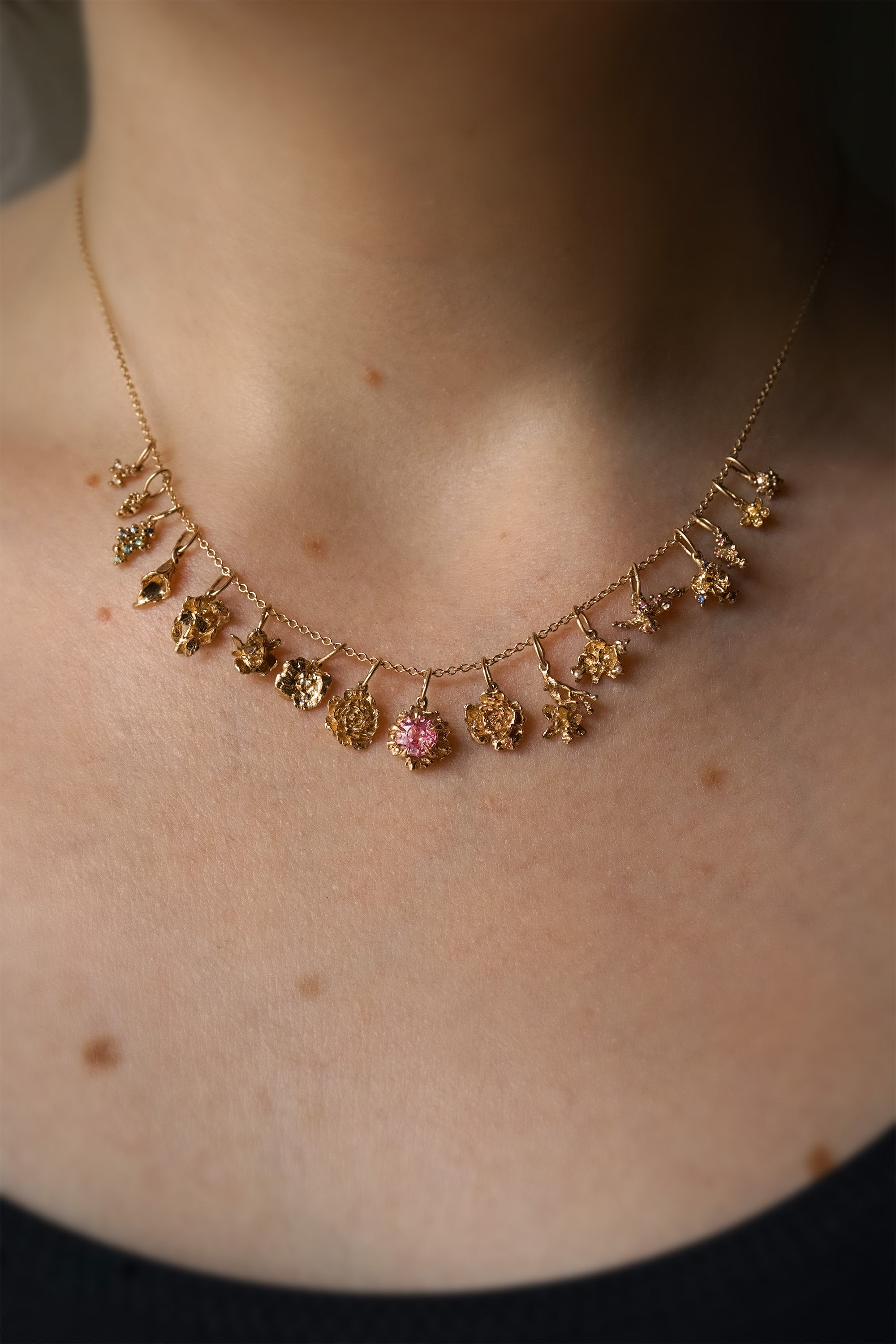 A close-up of a neck wearing a fine, 16 inch cable chain. On the chain are 17 handmade flower charms in solid gold with natural diamonds and sapphires, by Laurie Fleming Jewellery.