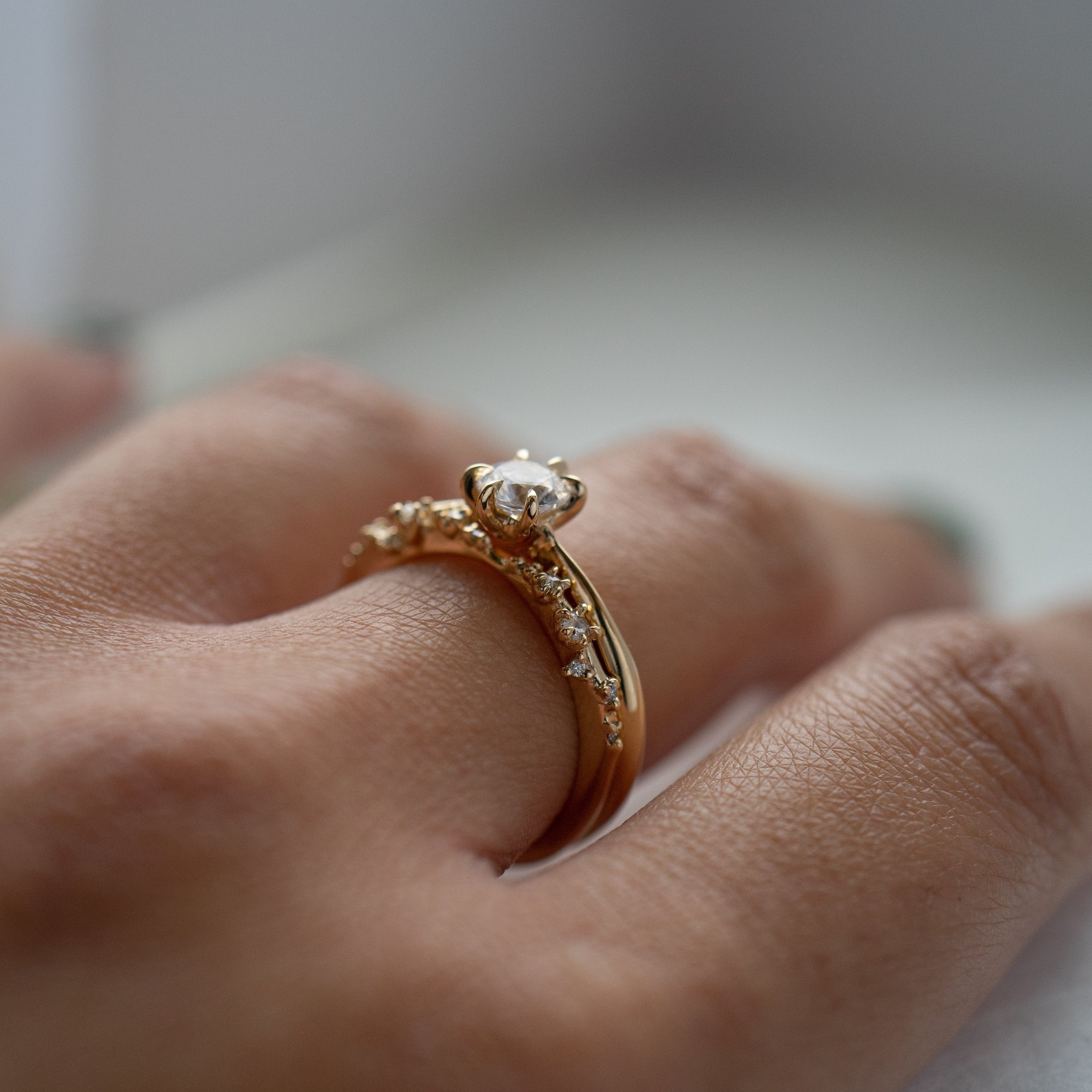 A photo of a hand wearing two Laurie Fleming Jewellery rings. The angle is from the side so you can better see the profile of both rings. Closest to the camera is the White Wisp band with small diamond accents, and above that is the Aurelia Ring with a half carat round brilliant cut diamond centre and a plain solid gold band.