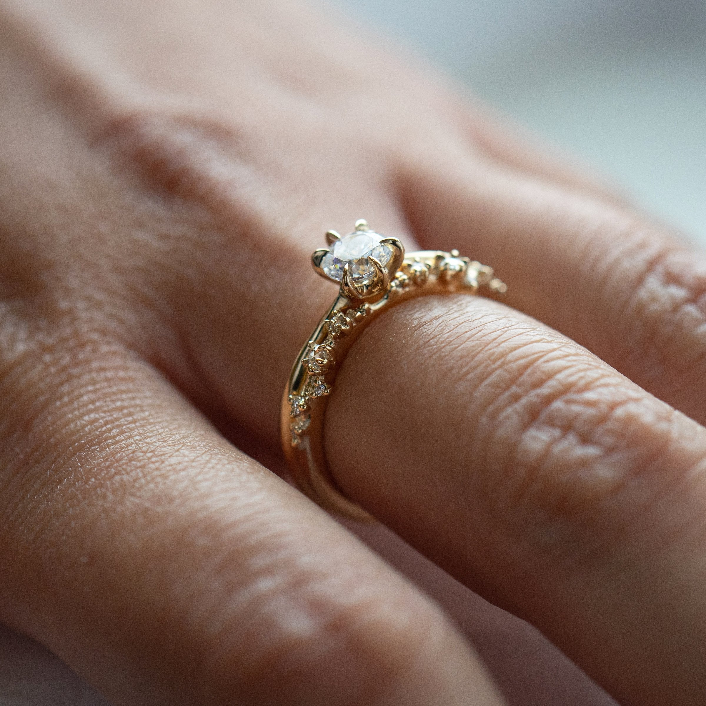 A photo of a hand wearing two Laurie Fleming Jewellery rings. The angle is from the side so you can better see the profile of both rings. Closest to the camera is the White Wisp band with small diamond accents, and above that is the Aurelia Ring with a half carat round brilliant cut diamond centre and a plain solid gold band.