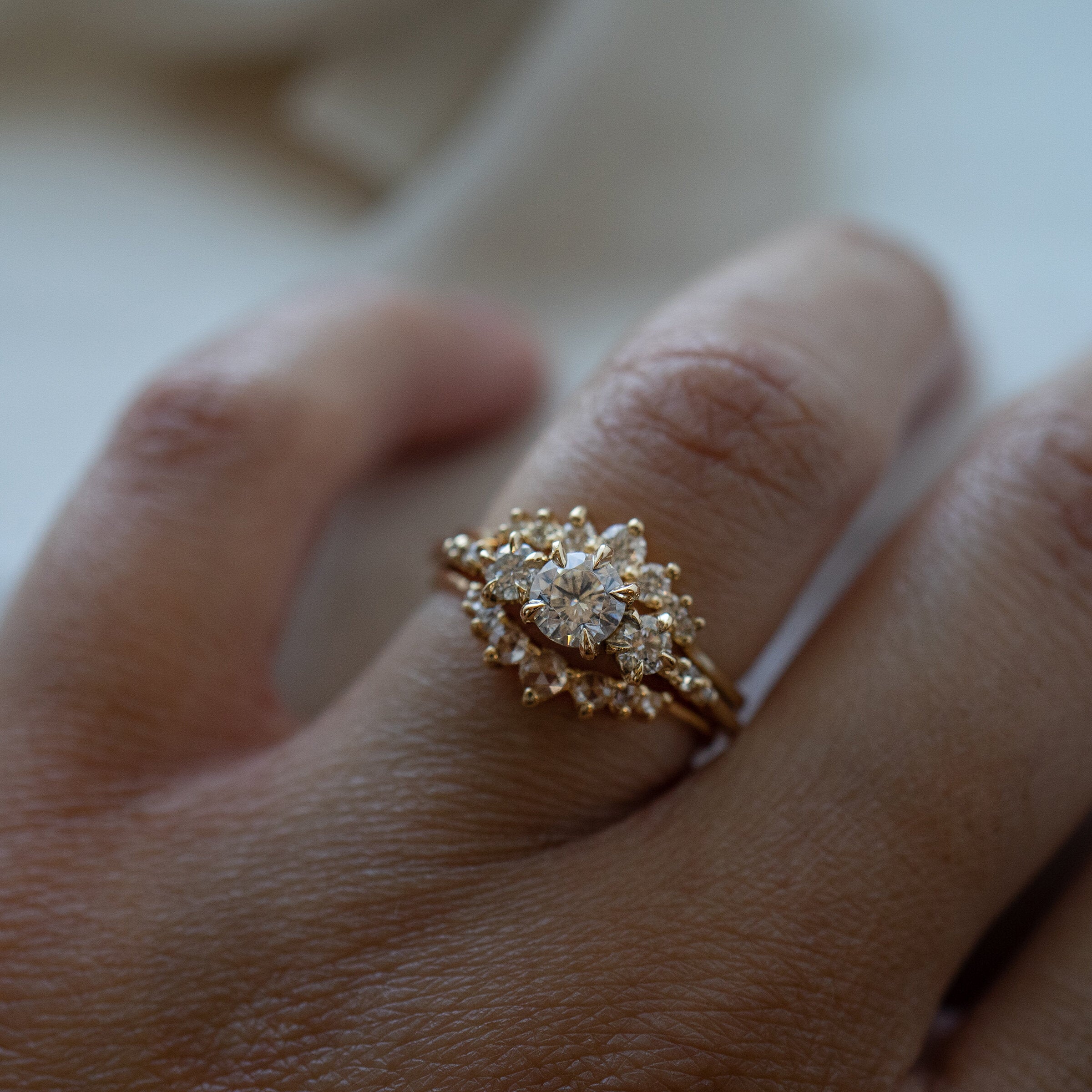 A hand wearing a stack of Laurie Fleming Jewellery rings. On top is the Brilliant Beacen ring, a gently contoured band with tapered sizes of round brilliant cut diamonds. In the middle is a Wild Iris three stone engagement ring, and on the bottom is a Rose Cut Diamond Beacen ring.