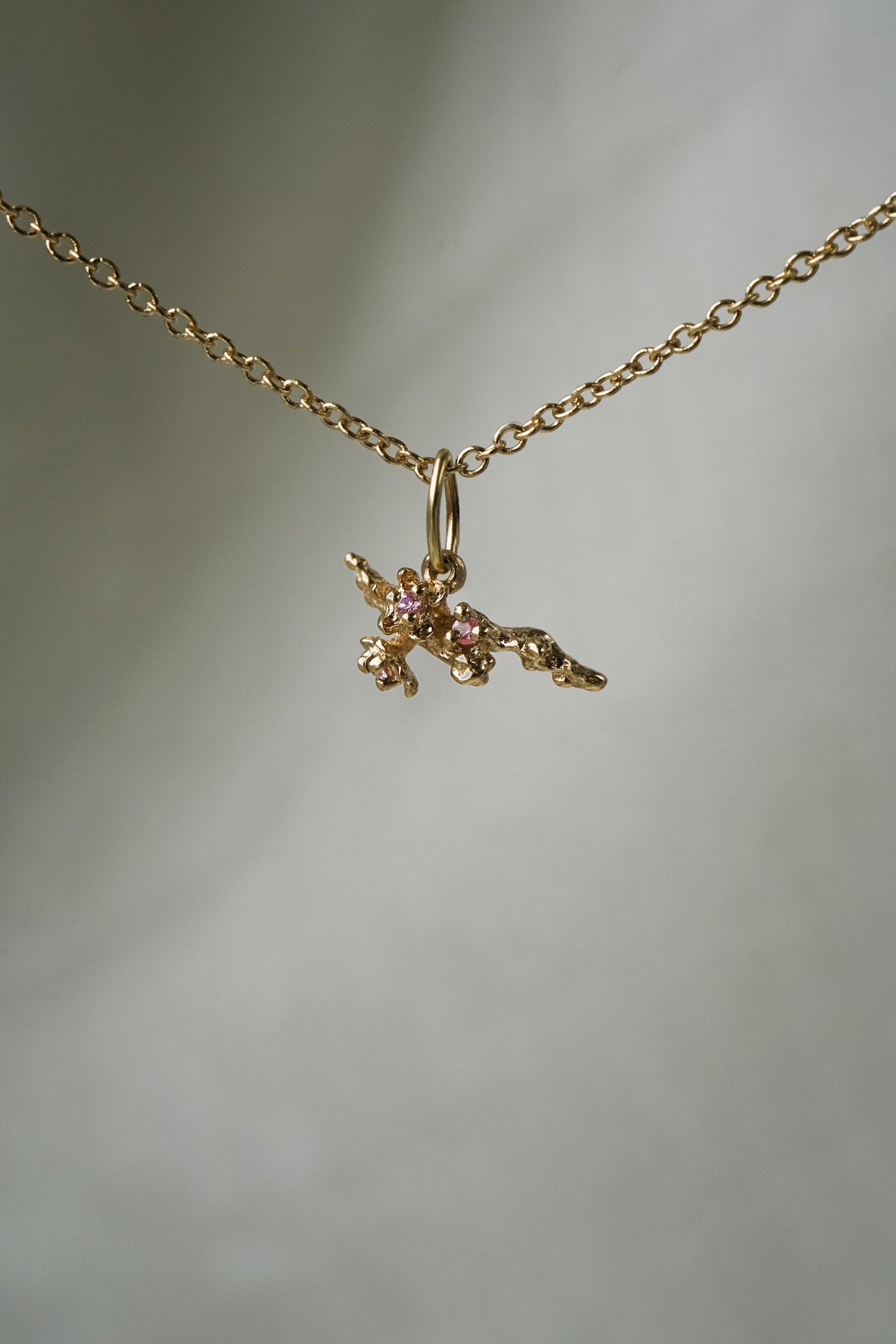 A delicate, hand-carved cherry blossom branch charm with pink sapphire blooms,  hanging from a 1mm cable chain with smooth oval links. Handmade in Toronto by Laurie Fleming Jewellery.