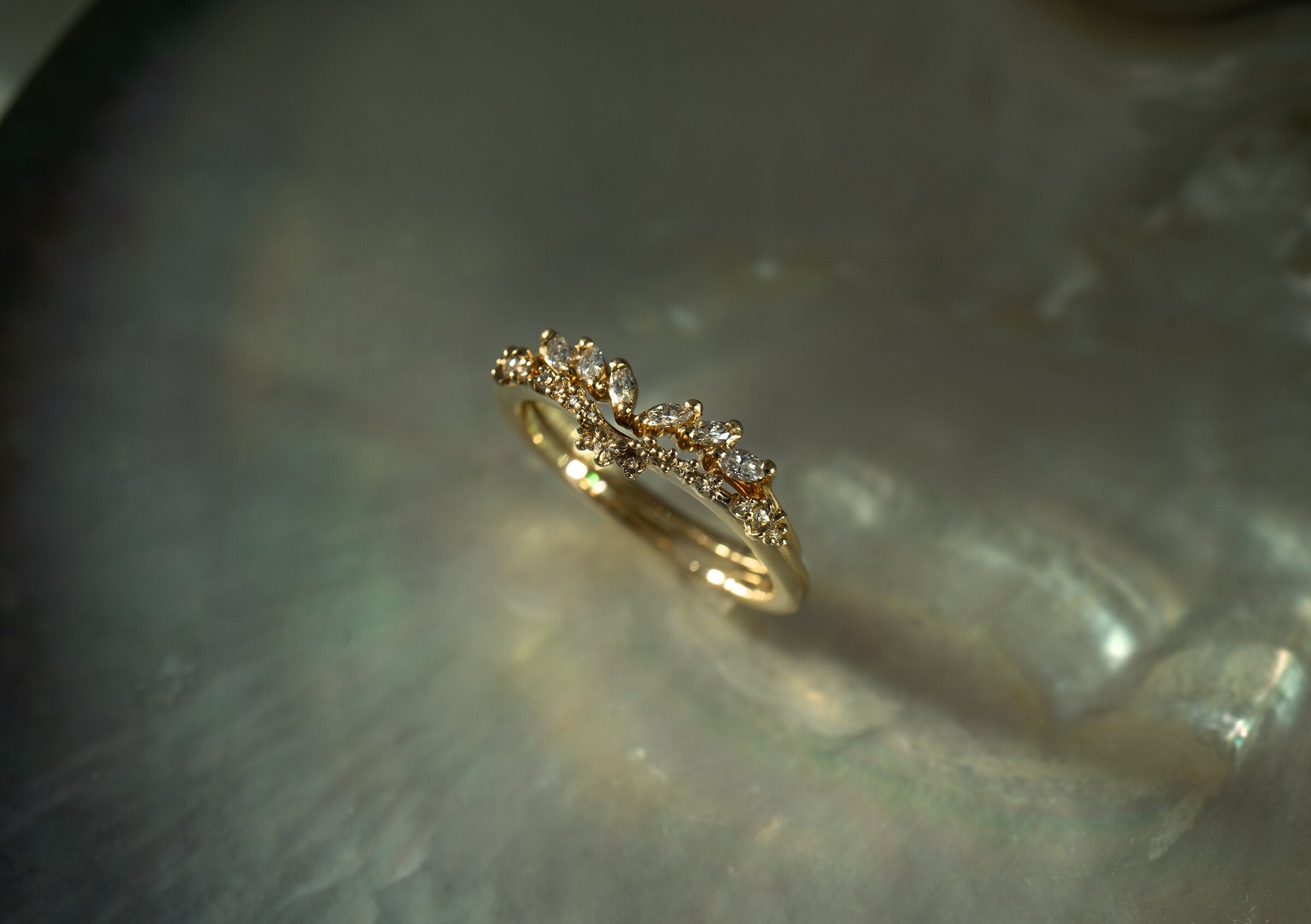 A close up of two rings held nestled together standing on an oyster dish. The top ring is a diamond Jasmine ring featuring marquise cut diamonds on the band and a gently pointed centre. The centre fits perfectly into the subtle dip of the Sylph band, which features rose cut and round brilliant cut diamonds along the band. Both rings are solid gold and handcarved by Laurie Fleming Jewellery.