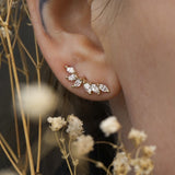 A close up of an ear wearing a Lyrie stud earring with six marquise cut diamonds. There are dried flower stems in the foreground around the ear.