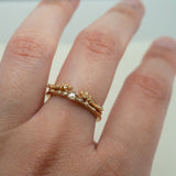 A stack of Laurie Fleming Jewellery rings worn on a hand. At the base of the finger is a "Water Lily Ring," a delicate solid gold stacking ring with round brilliant and rose cut diamonds scattered along the band. On top of that is a "Daphne Band", an open band that features clusters of both round brilliant and rose cut diamonds in varying sizes. The hand is in front of a pale grey background.