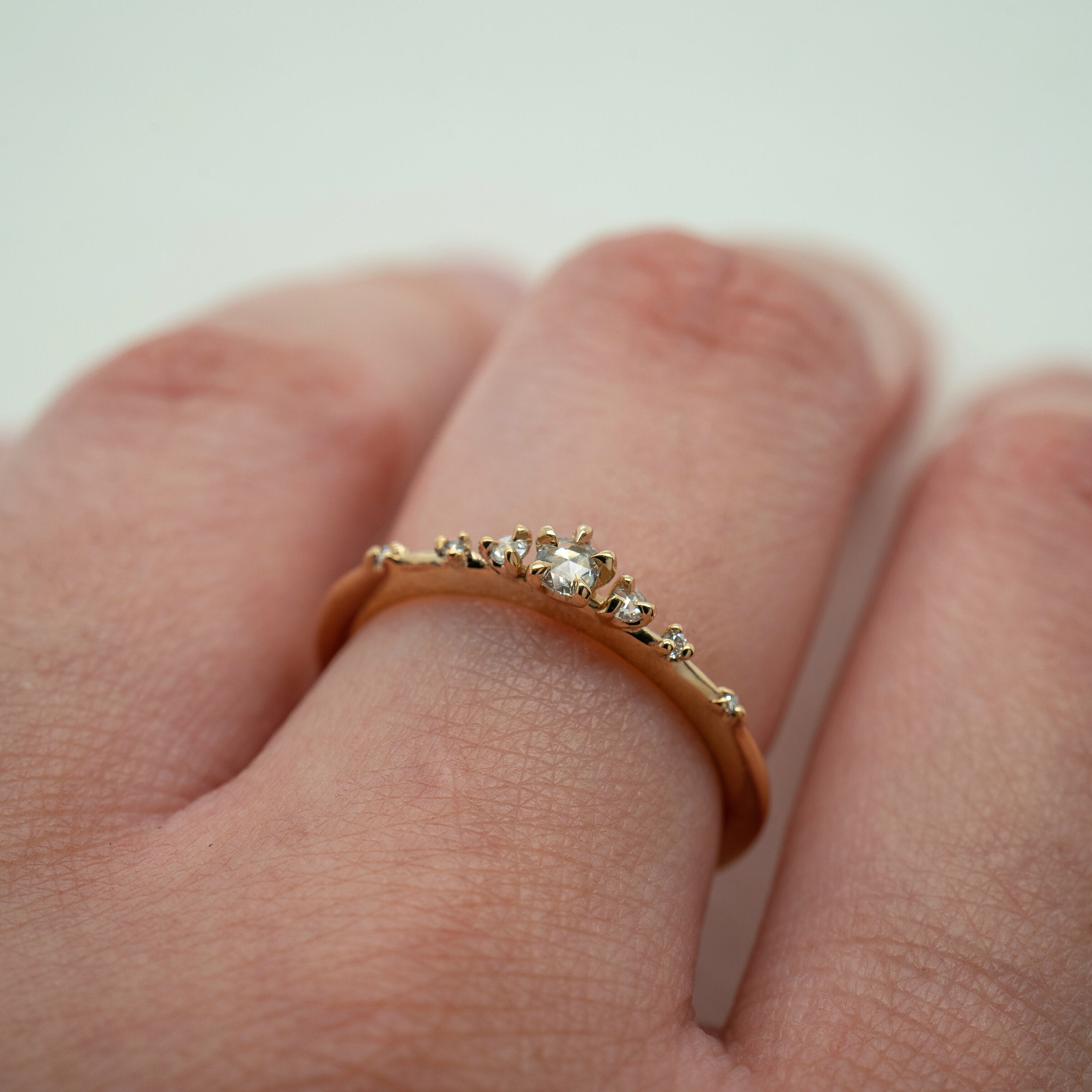 Laurie Fleming Jewellery's "Water Lily Ring," a delicate solid gold stacking ring with round brilliant and rose cut diamonds scattered along the band. The ring is worn on a hand in front of a pale grey background.