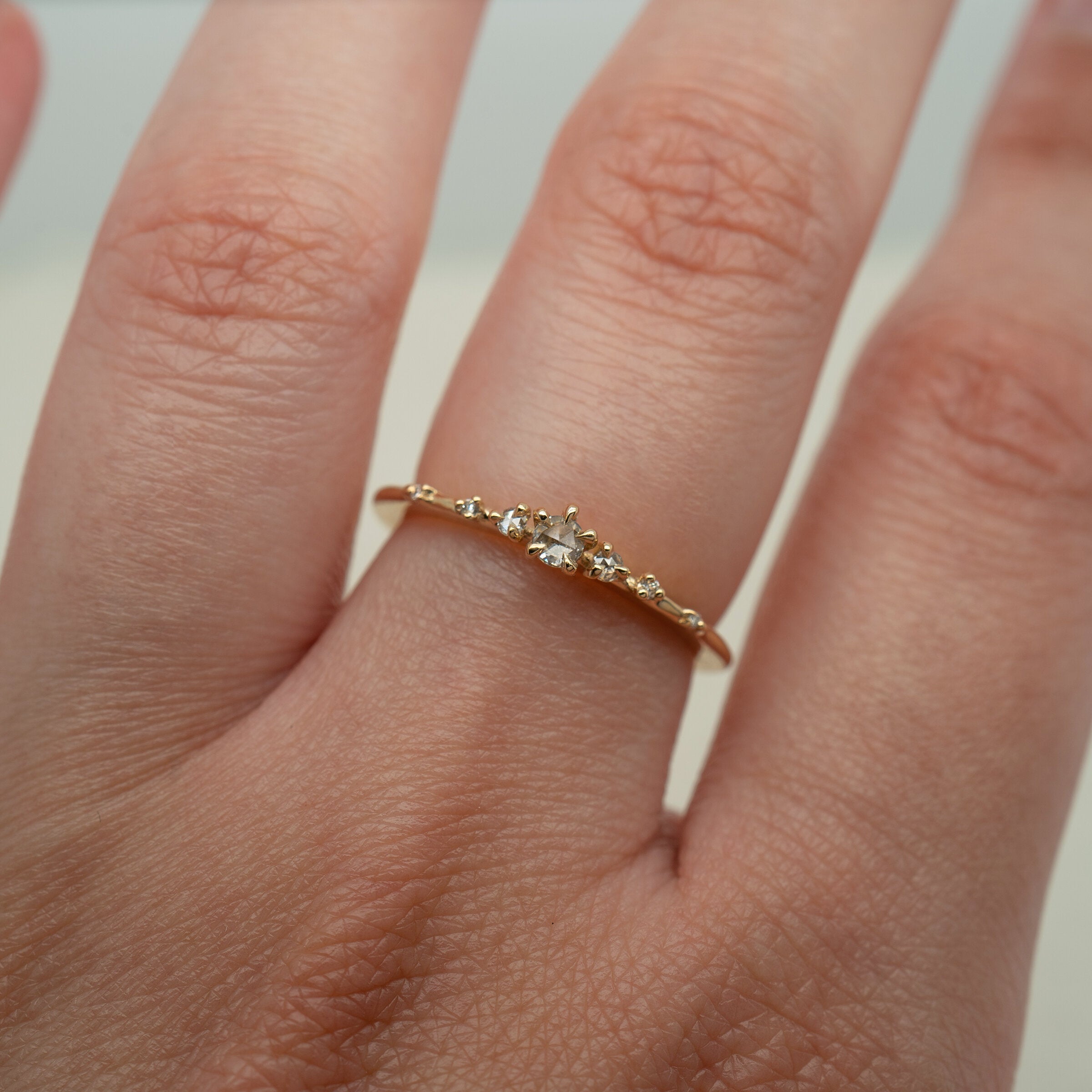 Laurie Fleming Jewellery's "Water Lily Ring," a delicate solid gold stacking ring with round brilliant and rose cut diamonds scattered along the band. The ring is worn on a hand in front of a pale grey background.