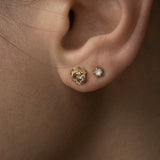 A close-up of an ear wearing two stud earrings by Laurie Fleming Jewellery. The model has tan skin and both earrings are in lobe piercings. The bottom piercing features a diamond Pansy stud, and the top piercing features a rose cut mother of pearl moondew stud.