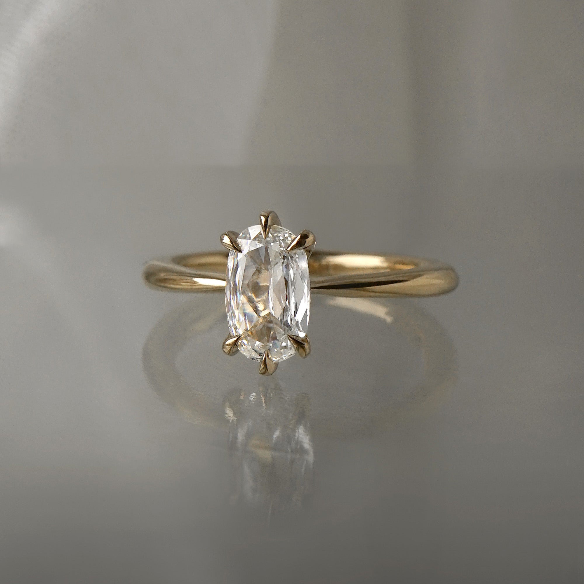 A one of a kind "Aurelia" style ring by Laurie Fleming Jewellery, featuring a unique elongated oval diamond with antique-inspired facets, on a gently tapered and rounded solid gold band. The ring is situated against a medium grey background.