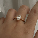 A one of a kind "Aurelia" style ring by Laurie Fleming Jewellery, featuring a unique elongated oval diamond with antique-inspired facets, on a gently tapered and rounded solid gold band. The ring is worn on a hand posed in front of some draped gossamer silk fabric.