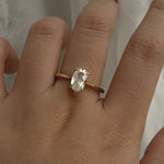 A one of a kind "Aurelia" style ring by Laurie Fleming Jewellery, featuring a unique elongated oval diamond with antique-inspired facets, on a gently tapered and rounded solid gold band. The ring is worn on a hand posed in front of some draped gossamer silk fabric.