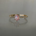 A delicate hand-carved one of a kind "Ilona" style engagement ring by Laurie Fleming Jewellery. The ring features a silky and opalescent rose cut oval pink sapphire centre, a tapered knife-edge band, and small diamond accents on the band shoulders.  The ring is situated against a medium grey background.