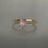 A delicate hand-carved one of a kind "Ilona" style engagement ring by Laurie Fleming Jewellery. The ring features a silky and opalescent rose cut oval pink sapphire centre, a tapered knife-edge band, and small diamond accents on the band shoulders.  The ring is situated against a medium grey background.