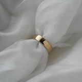 A stock photo of Laurie Fleming Jewellery's plain solid gold "Juniper" band, a 5mm wide flat comfort fit stacking ring/wedding band, handmade in Toronto. The ring is held on a roll of white silk fabric which is nestled against more silk.