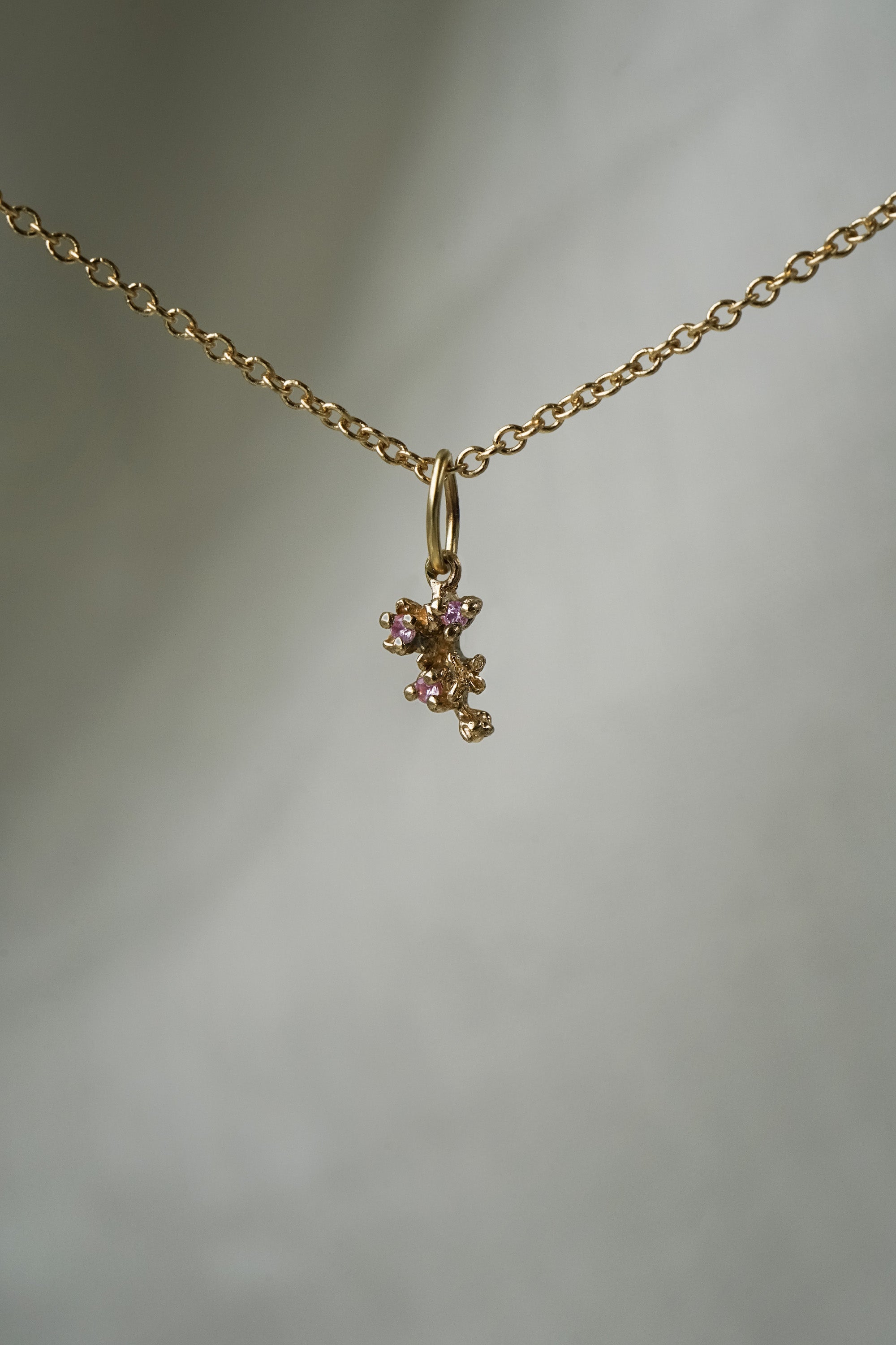 A miniature cluster of lilac flowers with pink sapphires in a charm,  hanging from a 1mm cable chain with smooth oval links. Handmade in Toronto by Laurie Fleming Jewellery.