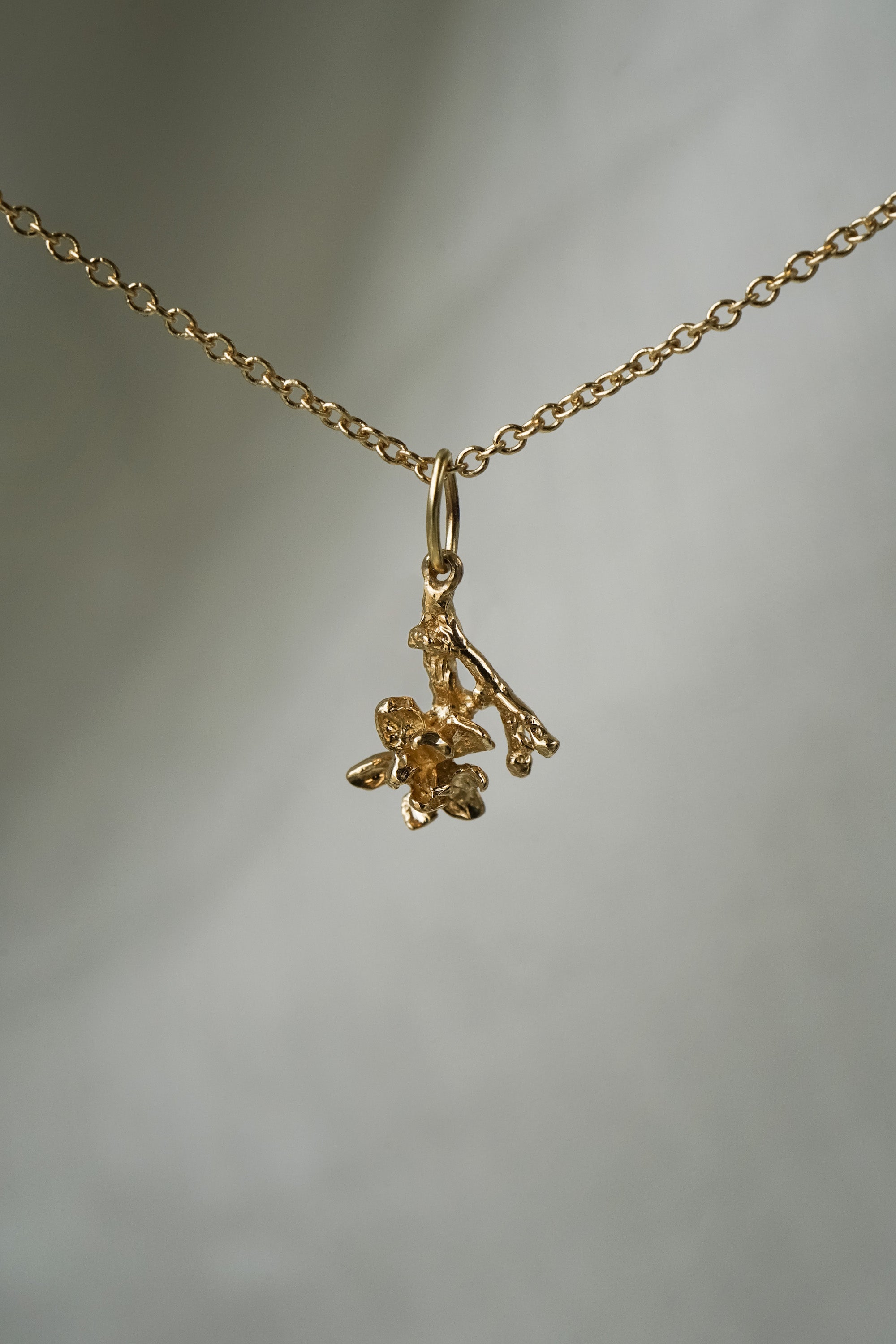 A hanging Magnolia branch charm, with one blooming flower,  hanging from a 1mm cable chain with smooth oval links. Handmade in Toronto by Laurie Fleming Jewellery.