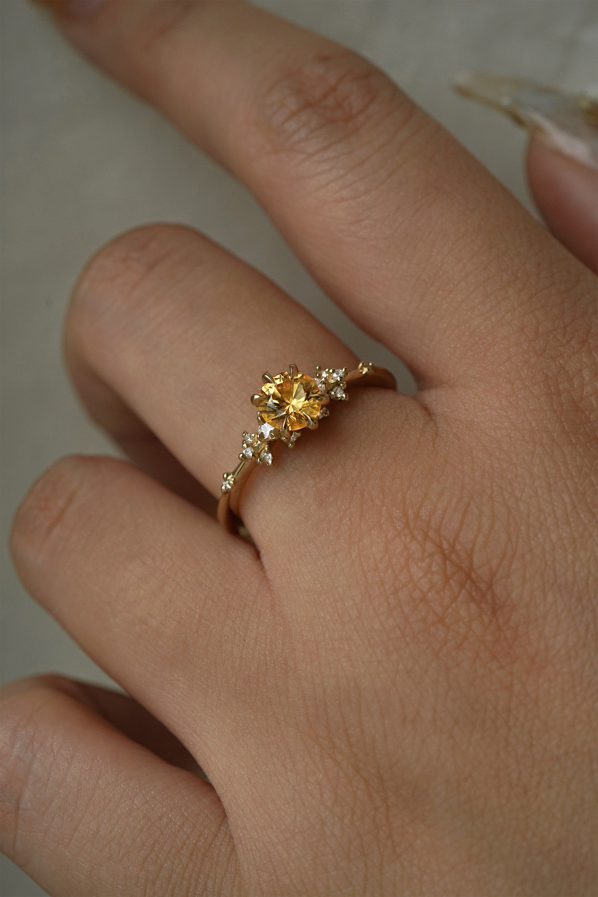 A hand wearing a one of a kind 18k yellow gold Water Lily engagement ring with a bright yellow round Montana sapphire centre with clusters of diamonds on the band.