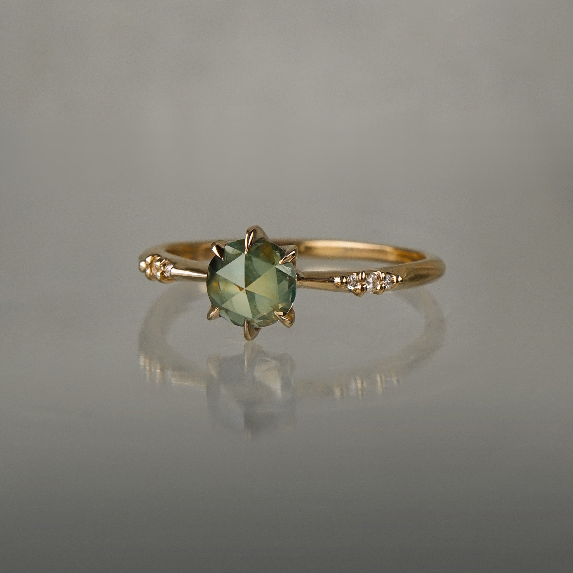 Dainty yellow gold Ilona style engagement ring by Laurie Fleming Jewellery on a grey background, with a rose cut green sapphire and diamonds on the band.