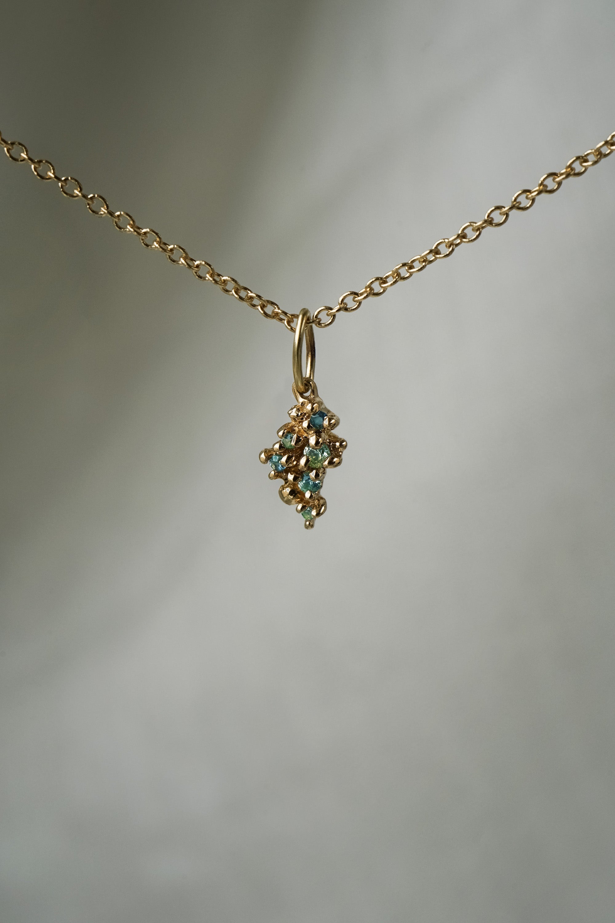 A patch of moss charm, featuring a cluster of blue-green teal sapphires,  hanging from a 1mm cable chain with smooth oval links. Handmade in Toronto by Laurie Fleming Jewellery.