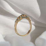 Laurie Fleming Jewellery's "Moss Signet Ring," a bold solid gold signet-style ring encrusted with varying shades and sizes of blue-green teal sapphires on the band.