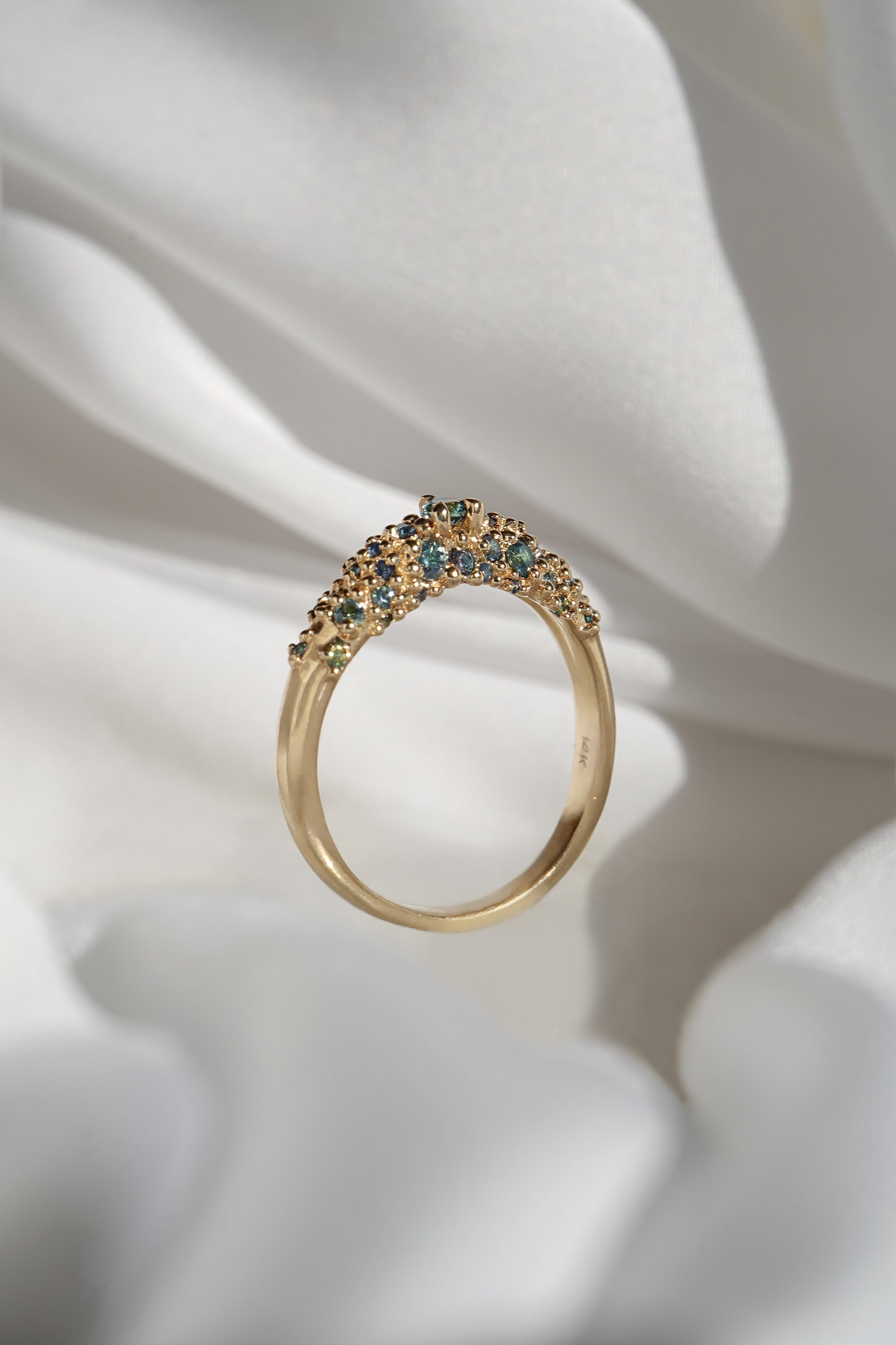 Laurie Fleming Jewellery's "Moss Signet Ring," a bold solid gold signet-style ring encrusted with varying shades and sizes of blue-green teal sapphires on the band.