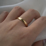 A stock photo of Laurie Fleming Jewellery's plain solid gold "Oak" band, a 3.5mm wide half round stacking ring/wedding band, handmade in Toronto. The ring is worn on a hand with a light grey background.