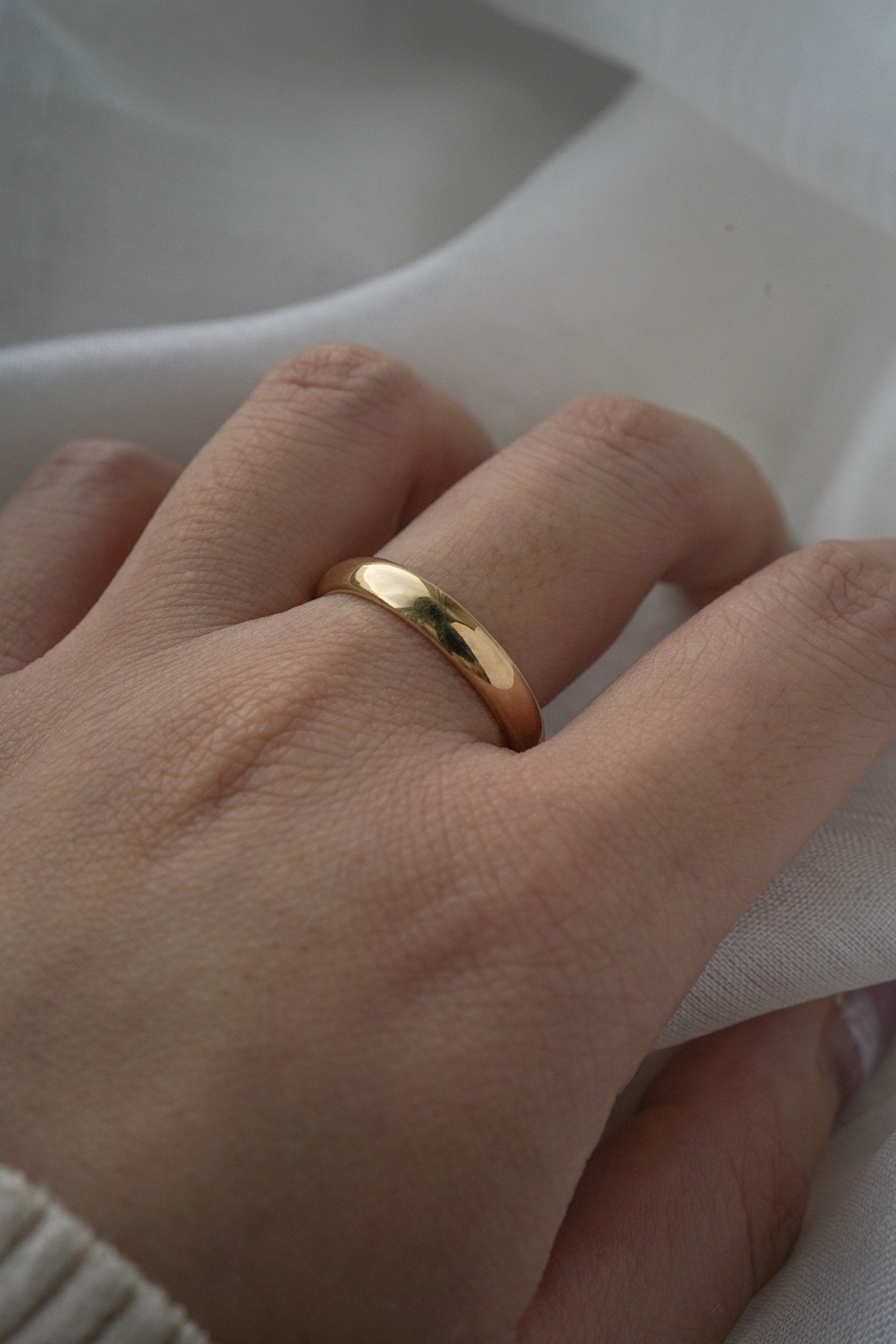 A stock photo of Laurie Fleming Jewellery's plain solid gold "Oak" band, a 3.5mm wide half round stacking ring/wedding band, handmade in Toronto. The ring is worn on a hand with a light grey background.