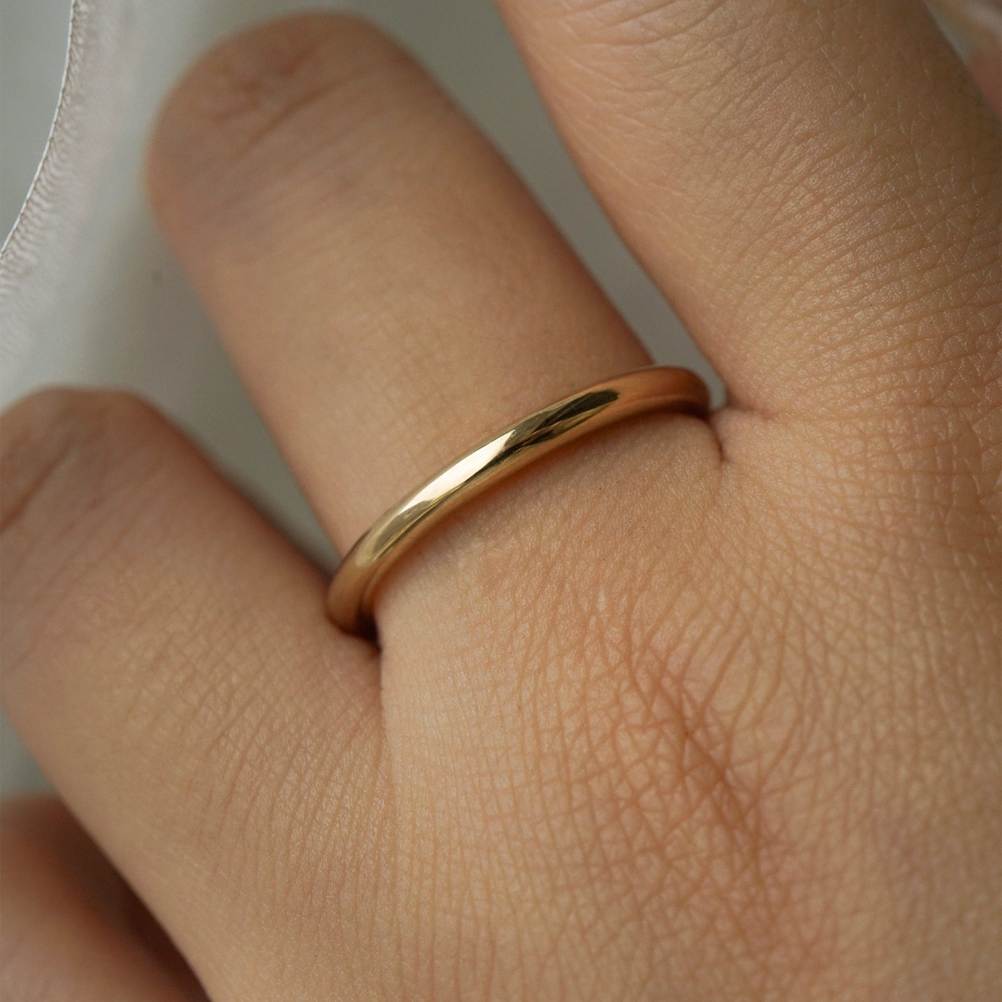A stock photo of Laurie Fleming Jewellery's plain solid gold "Peach" band, a 2.1mm wide round wire stacking ring/wedding band, handmade in Toronto. The ring is worn on a hand with a light grey background.