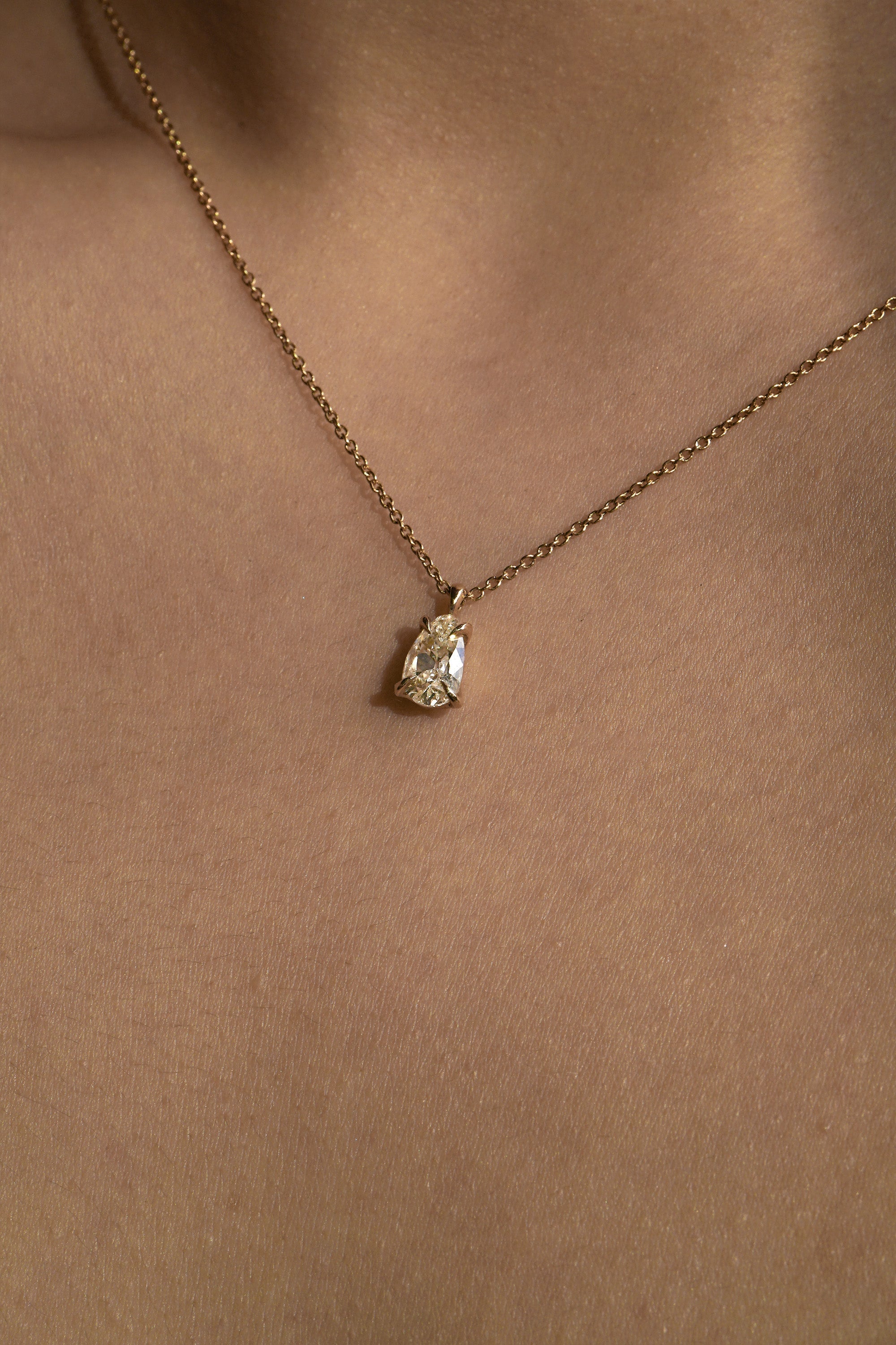 A photo of a one of a kind, handcarved solid 14k yellow gold necklace featuring a 1.07ct antique pear cut champagne diamond. The diamond is held in four delicate claw-shaped prongs. The pendant hangs from an adjustable 16-18" chain, and is shown worn on a tanned neck.