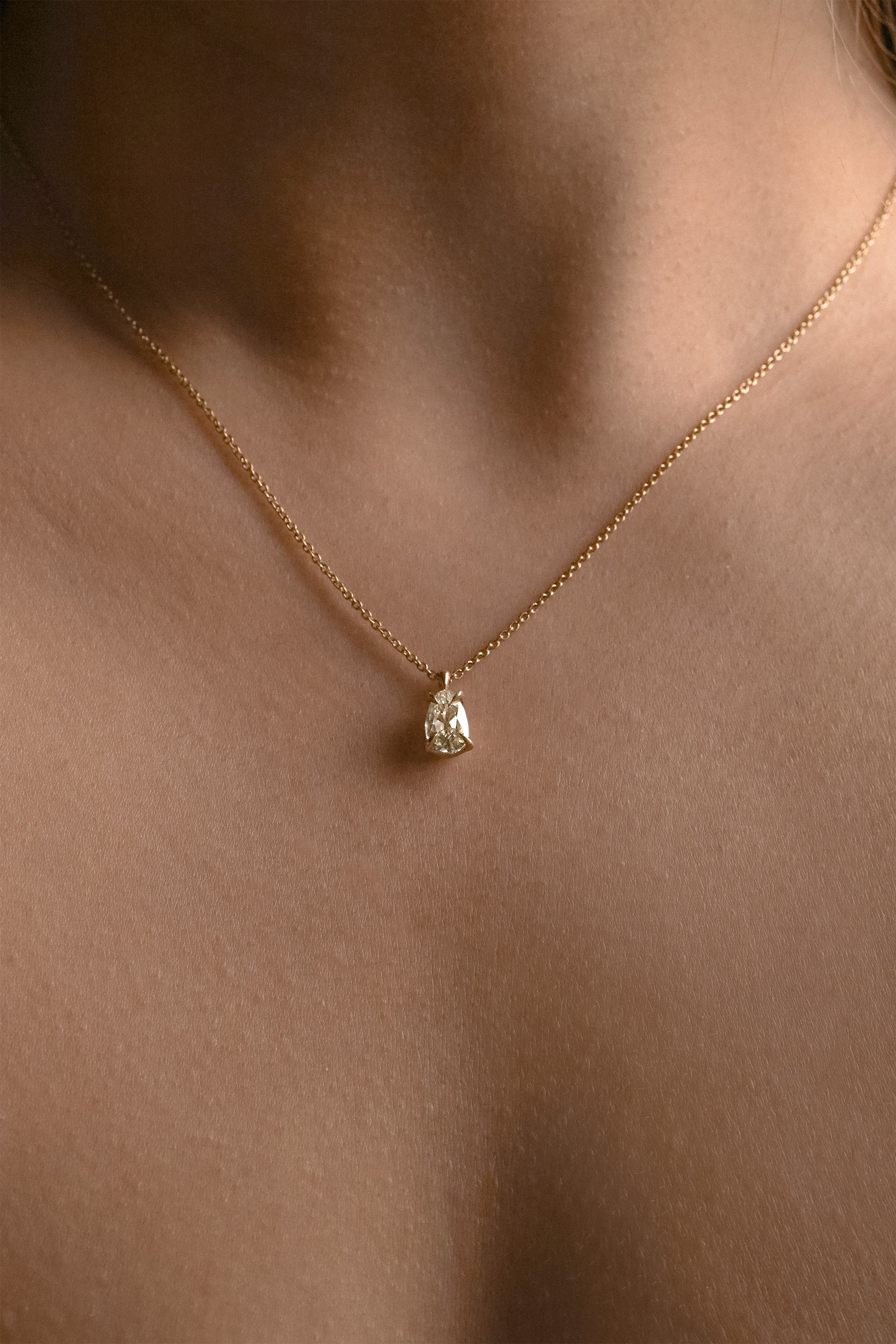 A photo of a one of a kind, handcarved solid 14k yellow gold necklace featuring a 1.07ct antique pear cut champagne diamond. The diamond is held in four delicate claw-shaped prongs. The pendant hangs from an adjustable 16-18" chain, and is shown worn on a tanned neck.