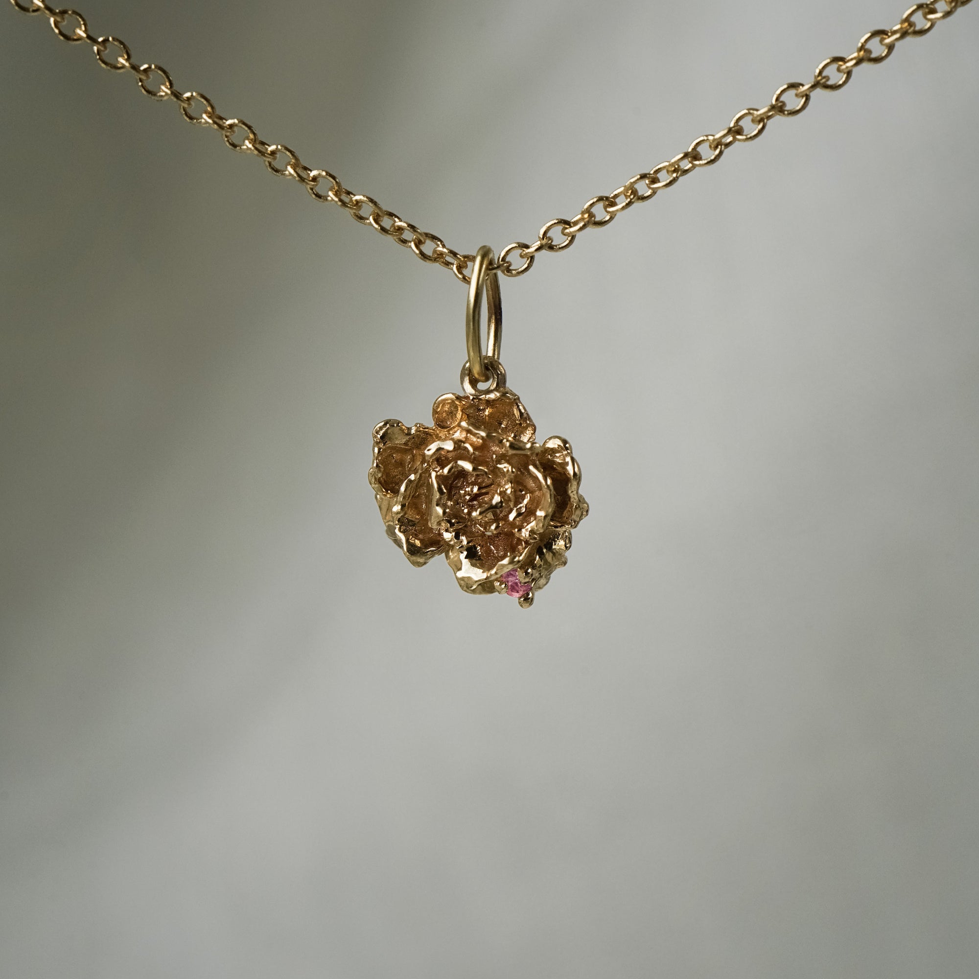 A hand-carved sculptural peony flower charm with a single pink sapphire,  hanging from a 1mm cable chain with smooth oval links. Handmade in Toronto by Laurie Fleming Jewellery.