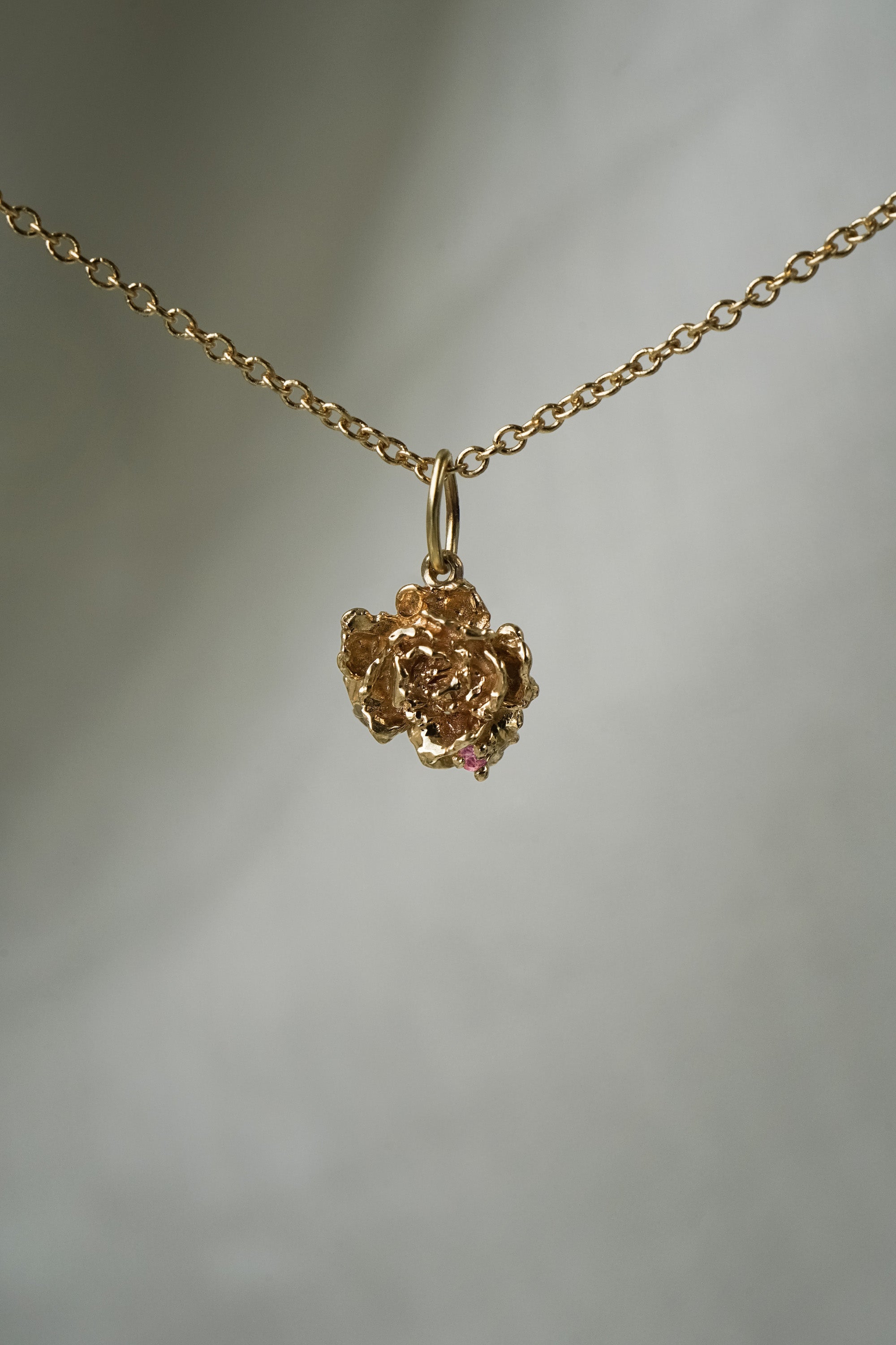 A hand-carved sculptural peony flower charm with a single pink sapphire,  hanging from a 1mm cable chain with smooth oval links. Handmade in Toronto by Laurie Fleming Jewellery.