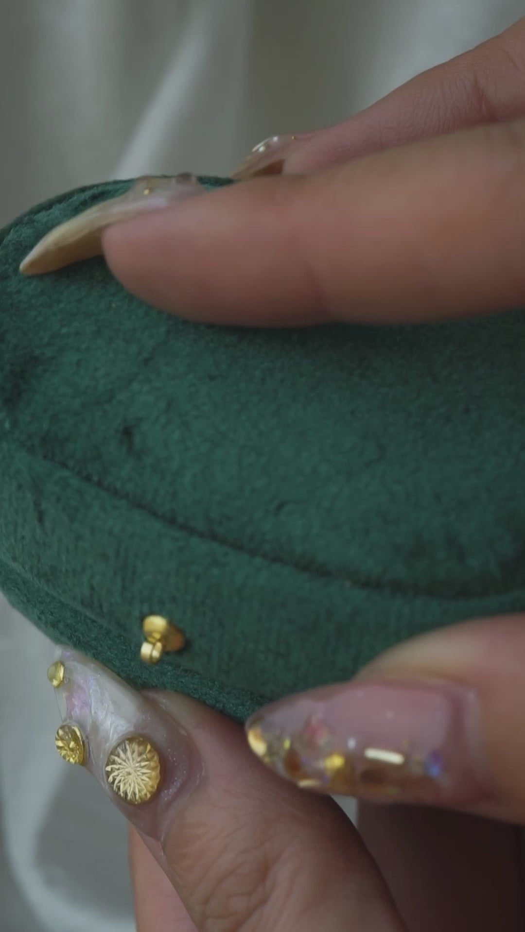 A green velvet box opens to reveal a solid gold handcarved Pansy floral signet by Laurie Fleming Jewellery; The ring is held in pliers and rotated at various angles; the ring is placed on a finger.