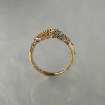 Laurie Fleming Jewellery's "Rainbow Sapphire Moss Signet Ring," a bold solid gold signet-style ring encrusted with sapphires in varying shades and sizes in deep pink, medium pink, light pink, orange, yellow, green, blue-green, medium blue, light blue, and purple, with a single round brilliant cut diamond at the centre on the band. The ring is seen from a side view in front of a medium grey background.