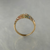 Laurie Fleming Jewellery's "Rainbow Sapphire Moss Signet Ring," a bold solid gold signet-style ring encrusted with sapphires in varying shades and sizes in deep pink, medium pink, light pink, orange, yellow, green, blue-green, medium blue, light blue, and purple, with a single round brilliant cut diamond at the centre on the band. The ring is seen from a side view in front of a medium grey background.