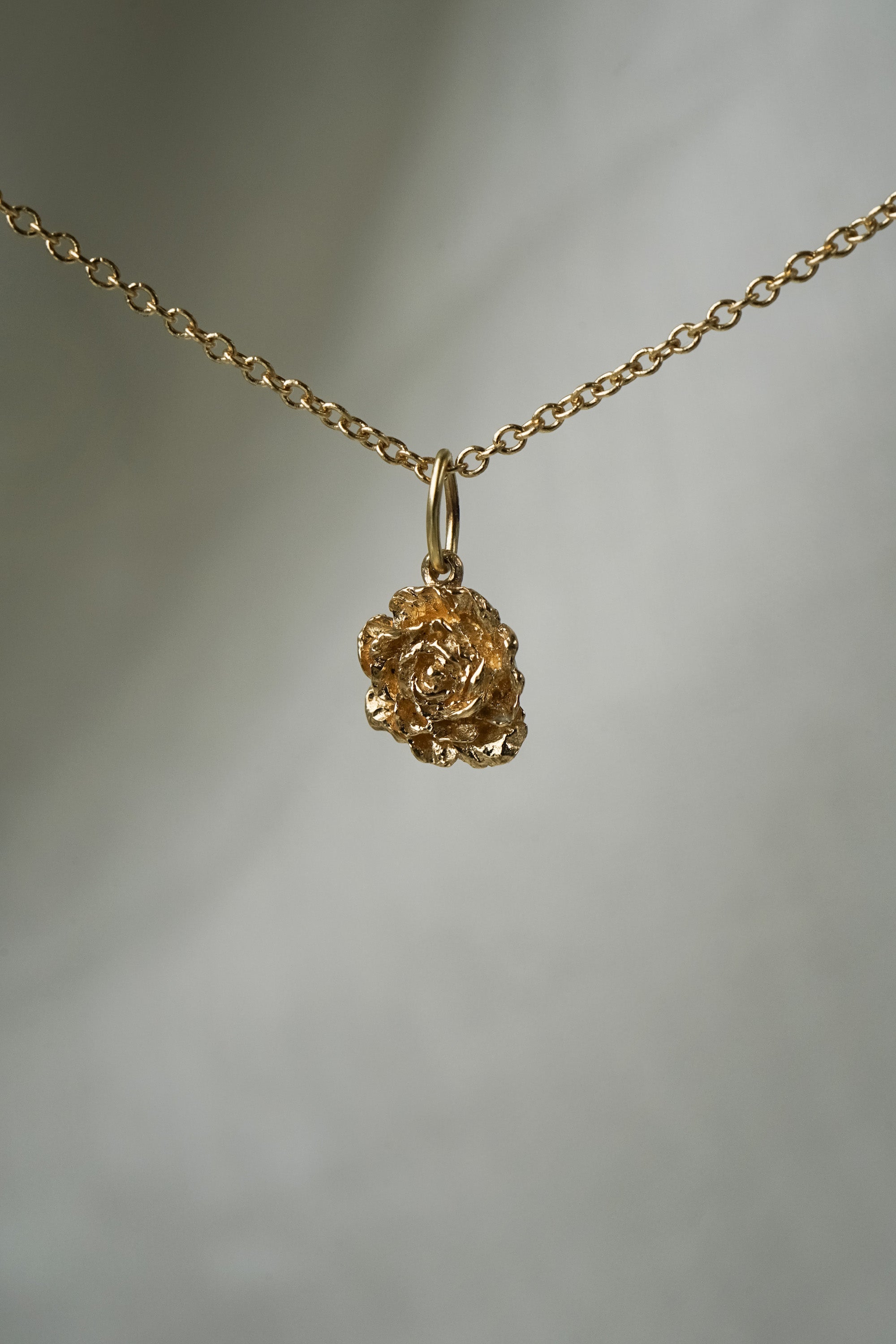 A hand-carved ranunculus flower charm,  hanging from a 1mm cable chain with smooth oval links. Handmade in Toronto by Laurie Fleming Jewellery.