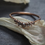 A product photo showing the salt and pepper rose cut diamond Beacen Ring by Laurie Fleming Jewellery. The ring features a gentle tapered curve that stacks well with other rings or contours against engagements rings. It is resting against a dried white flower petal on a grey background.