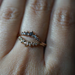 A close up of a hand wearing two solid gold contour band rings by Laurie Fleming Jewellery; on top, the rose cut Salt and Pepper Diamond Beacen ring, and on the bottom, the rose cut diamond Beacen ring.