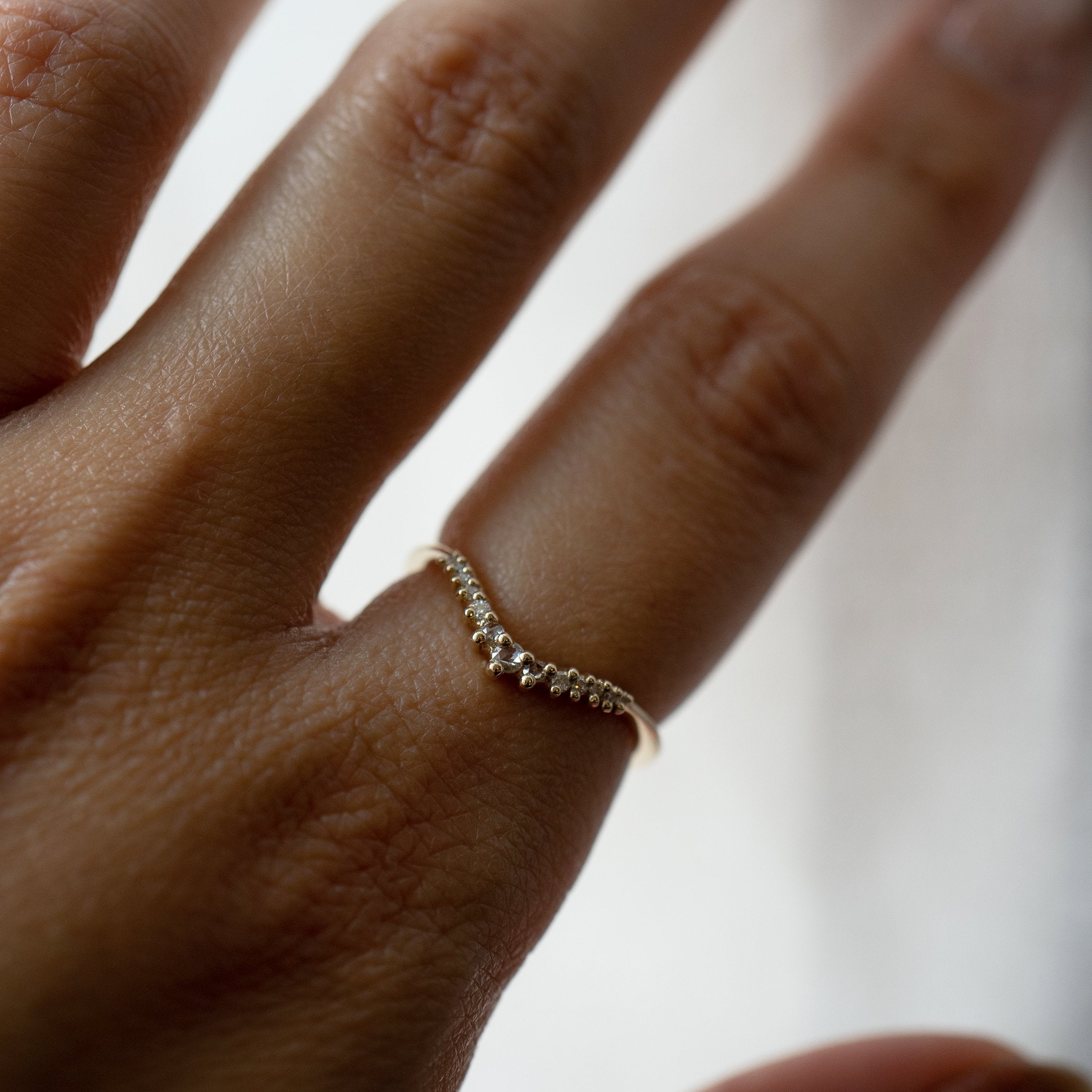 A close up of a hand wearing a solid gold Selene contour band ring by Laurie Fleming Jewellery, which features rose cut and brilliant cut diamonds along a curve to stack with other rings (such as with an engagement ring).