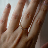 A close up of a hand wearing a solid gold Selene contour band ring by Laurie Fleming Jewellery, which features rose cut and brilliant cut diamonds along a curve to stack with other rings (such as with an engagement ring).