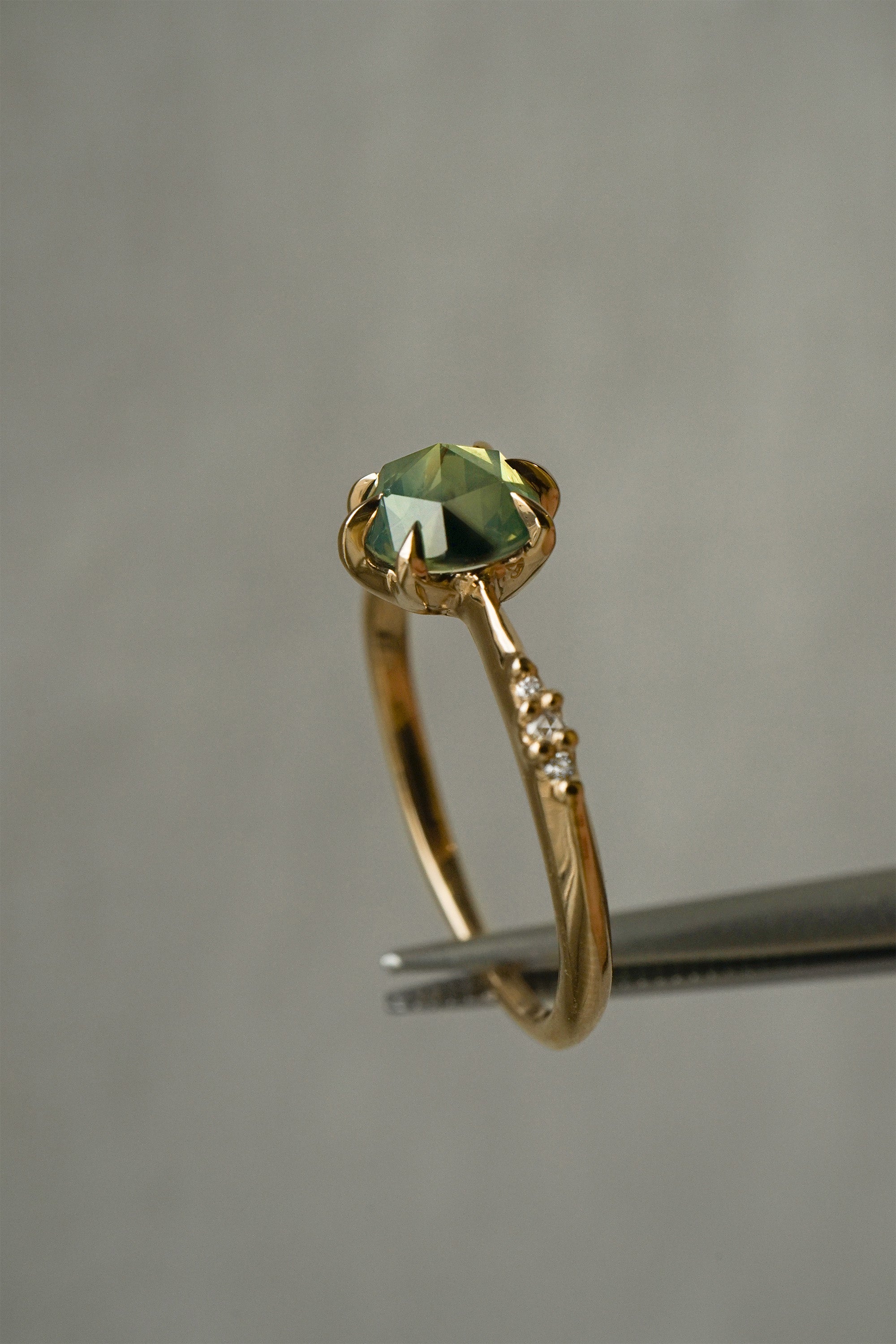 Dainty yellow gold Ilona style engagement ring by Laurie Fleming Jewellery on a grey background, with a rose cut green sapphire and diamonds on the band.