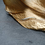 Hand-carved sculptural "Versare" earrings by Laurie Fleming Jewellery positioned on a gold leaf.