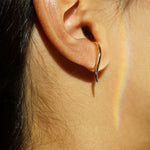 A close-up of an ear showing one of the possible ways to wear the hand-carved sculptural solid gold "Versare" earrings by Laurie Fleming Jewellery.