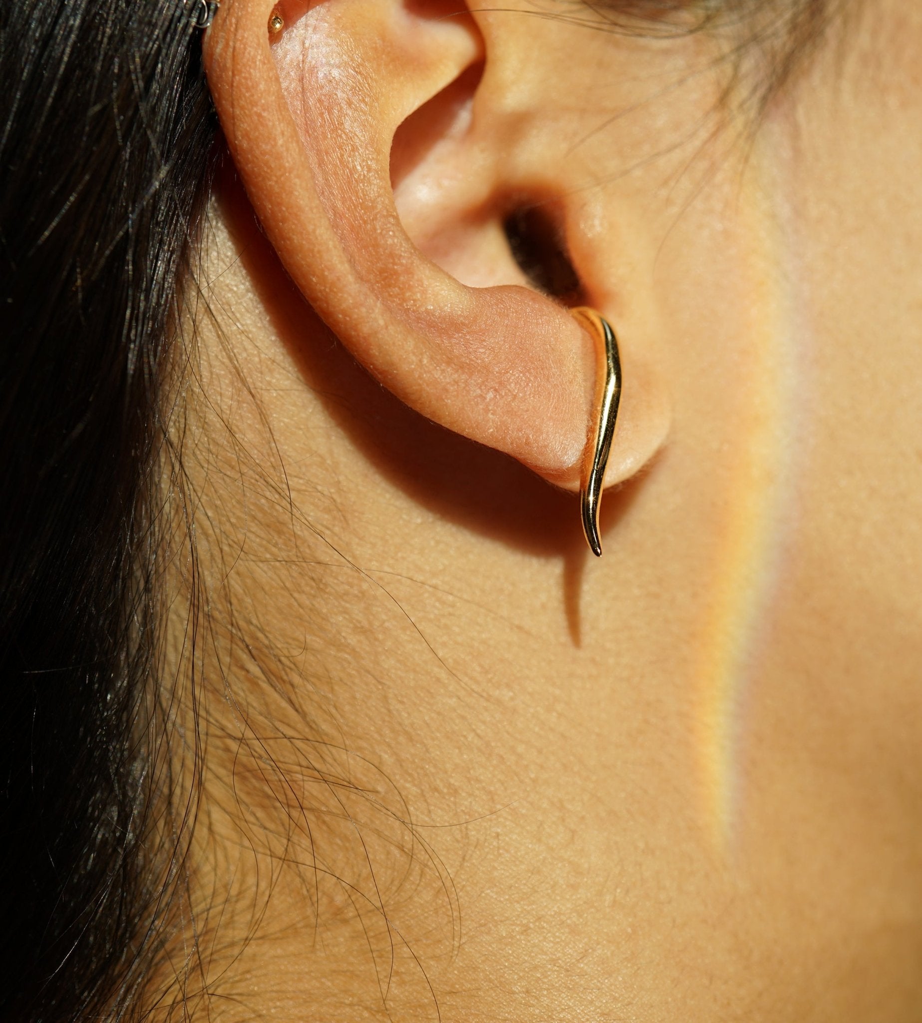 A close-up of an ear showing one of the possible ways to wear the hand-carved sculptural solid gold "Versare" earrings by Laurie Fleming Jewellery.