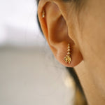 A close up of an ear wearing Laurie Fleming Jewellery's "White Orchid" earring, which features a hand-carved solid gold miniature orchid flower stud, and an optional ear jacket that curves up into the ear with tiny seed pearl accents.