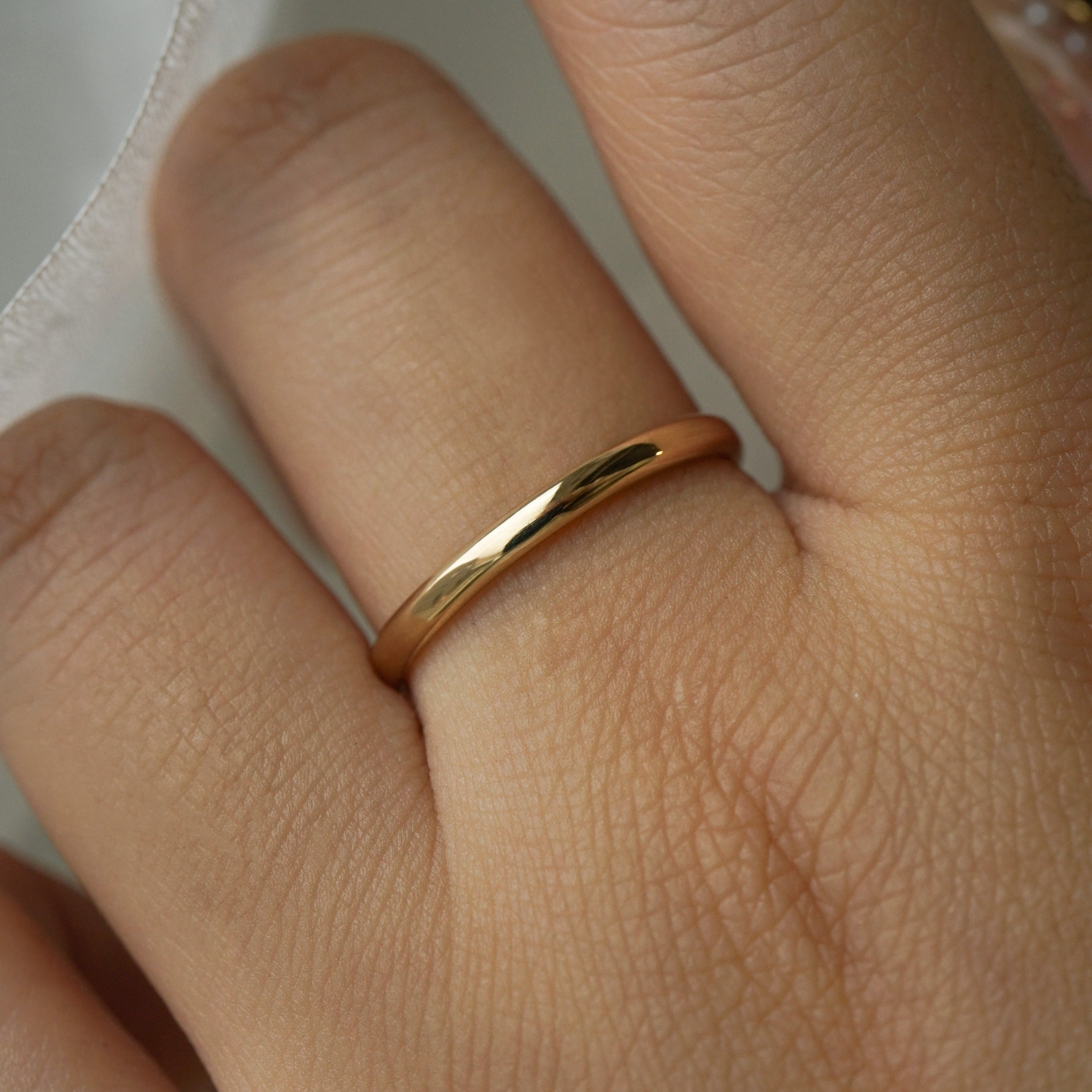 A stock photo of Laurie Fleming Jewellery's plain solid gold "Wisteria" band, a 2mm wide stacking ring/wedding band, handmade in Toronto. The ring is worn on a hand with a light grey background.